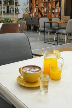 Sarı kahve fincanı, bir bardak portakal suyu ve bir bardak likör.