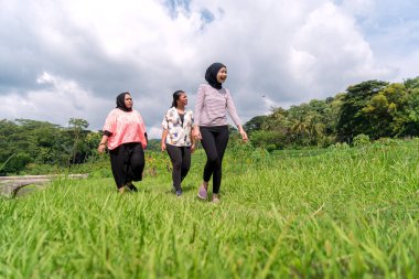Üç Asyalı kadın yemyeşil bir kanalda yürüyorlar güneşli bir günde doğa ve sohbetin tadını çıkarıyorlar..