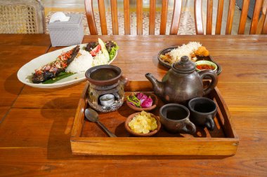 Geleneksel çay seti kil çaydanlık, fincanlar, kaya şekeri ve çay ısıtıcısı ahşap bir tepside, otantik bir kafe ortamında otantik çay kültürünü temsil ediyor..