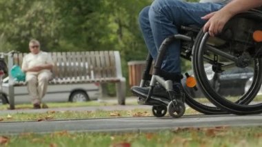 Tekerlekli sandalyedeki engelli adam parkta yürüyor.