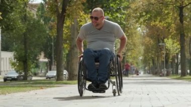 Parkta tekerlekli sandalyede yürüyen mutlu engelli adam.