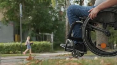 Tekerlekli sandalyedeki engelli adam parkta yürüyor.