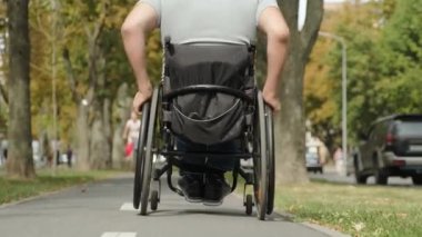 Tekerlekli sandalyedeki engelli adam parkta yürüyor.
