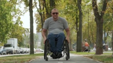 Tekerlekli sandalyedeki engelli adam parkta yürüyor.