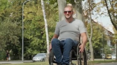 Tekerlekli sandalyedeki engelli adam parkta yürüyor.