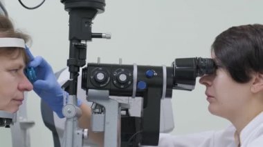 Kadın doktor göz doktorundan göz hekimliği kliniğindeki hastanın gözlerine bakıyor. Uzman vizyon denetimi