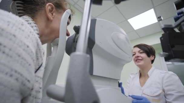 女性医師は眼科診療所の患者の目に眼科を通して見ています ビジョンの専門検査 — ストック動画