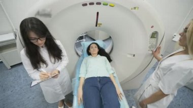 Kadın hasta, modern tıp kliniğinde iki kalifiye radyoloğun gözetiminde CT veya MRI taramasından geçiriliyor. Hasta tomografide ya da MRI tarama yatağında yatıyor, makinenin içinde hareket ediyor..