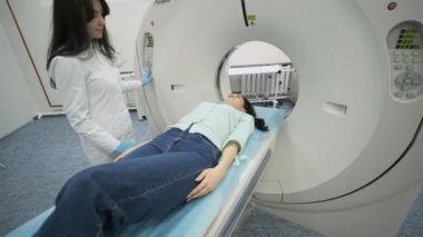 Kadın hasta, modern tıp kliniğinde bir radyologun gözetiminde CT ya da MRI taramasından geçiriliyor. Hasta tomografide ya da MRI tarama yatağında yatıyor, makinenin içinde hareket ediyor..