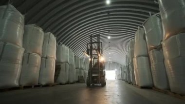 Depoda. Forklift sürücüsü depoya büyük bir çanta dolusu hammadde yığıyor. Depoda bir sürü hammadde var.