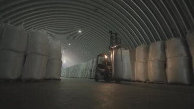 Depoda. Forklift sürücüsü depoya büyük bir çanta dolusu hammadde yığıyor. Depoda bir sürü hammadde var.