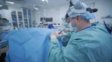 Ameliyathane, hasta derin anestezi altında, asistanı en son cihazları kullanan cerrah, soğuk plazma metodu, boğazda şişme, doktor yeni bir sonda, tıbbi far, cerrahi lenslerle çalışıyor.