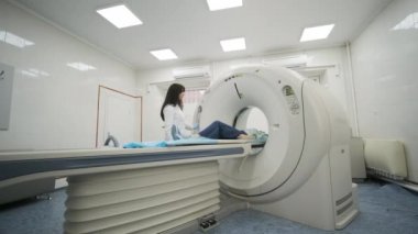 Kadın hasta, modern tıp kliniğinde bir radyologun gözetiminde CT ya da MRI taramasından geçiriliyor. Tomografide ya da MR tarama yatağında yatan hasta, makinenin dışına çıkıyor..