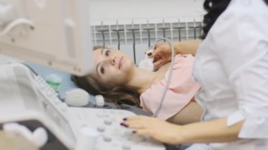 Klinikte genç kadın tiroid bezinin ultrason taraması yapılıyor. Kadın doktor hastanın boynunda ultrason sensörü çalıştırıyor..