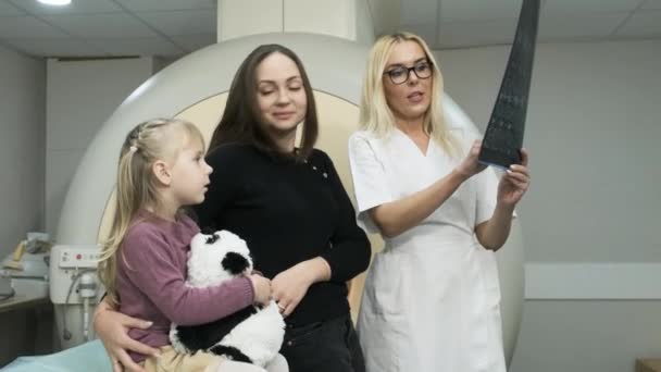 Női orvos radiológus elmagyarázza eredményeit MRI szkennelés nő a gyermekével, mutatja a pillanatfelvétel képekkel, megfigyelése és elemzése MRI modern klinikán mellett modern zárt típusú MRI — Stock videók