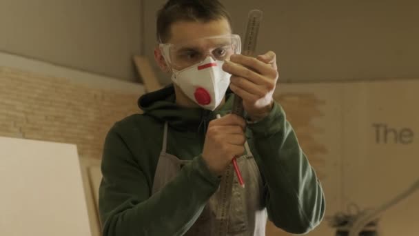 Trabajador carpintero profesional en máscara y gafas sosteniendo una regla y lápiz — Vídeo de stock