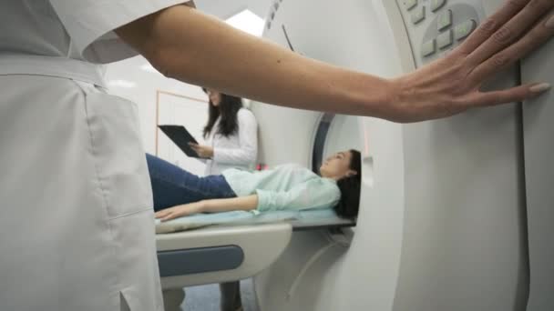 "La paciente femenina se somete a una tomografía computarizada o una resonancia magnética bajo la supervisión de dos radiólogos calificados en una clínica médica moderna. Paciente acostado en una mesa de tomografía computarizada o resonancia magnética — Vídeo de stock