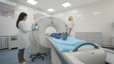 Female patient is undergoing CT or MRI scan under supervision of two qualified radiologists in modern medical clinic. Patient lying on a CT or MRI scan table, leaves the machine