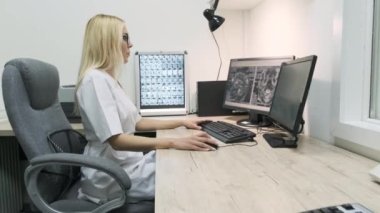 Profesyonel kadın radyoloji uzmanı beyin tomografisi ya da MRI sonuçlarını inceleyerek hastanedeki kişisel masasında bilgisayar ekranı üzerinde çalışıyor.