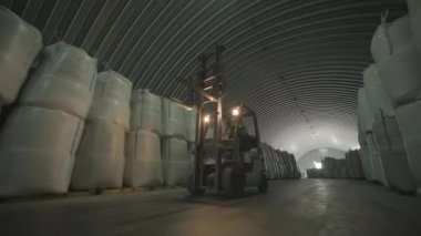 Depoda. Forklift sürücüsü depoya büyük bir çanta dolusu hammadde yığıyor. Depoda bir sürü hammadde var.