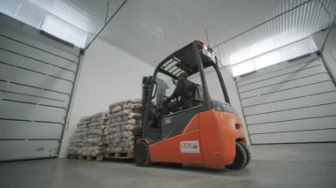 Depoda. Forklift sürücüsü depoya büyük bir çanta dolusu hammadde yığıyor. Depoda bir sürü hammadde var.
