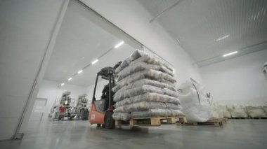 Depoda. Forklift sürücüsü depoya büyük bir çanta dolusu hammadde yığıyor. Depoda bir sürü hammadde var.