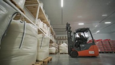 Depoda. Forklift sürücüsü depoya büyük bir çanta dolusu hammadde yığıyor. Depoda bir sürü hammadde var.