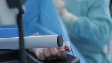 Operation of removing tonsils under deep anesthesia, using latest devices, cold plasma method, cuts swelling in throat, doctor works with new probe, medical headlamp, surgical loupes, patient with pulse oximeter on finger