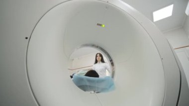Kadın hasta, modern tıp kliniğinde bir radyologun gözetiminde CT ya da MRI taramasından geçiriliyor. Hasta tomografide ya da MRI tarama yatağında yatıyor, makinenin içinde hareket ediyor..