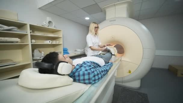 女医生做膝关节Mri扫描 坐在自动桌子上的年轻男性患者使用隔音耳机进入一种密闭式Mri机器 现代设备 病人膝盖上的线圈 — 图库视频影像