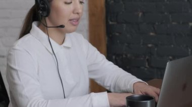 Kadın çağrı merkezi operatörü, müşteri destek acentesi kulaklık takıyor, konsültasyon yapıyor, dizüstü bilgisayarda yazıyor, internette konuşuyor, yardım hattı operatörü konferans videosu çekiyor.