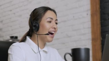 Gülümseyen kadın çağrı merkezi operatörü, müşteri destek ajanı kulaklık takıyor, danışmanlık yapıyor, dizüstü bilgisayarda yazıyor, internette konuşuyor, yardım hattı operatörü konferans videosu çekiyor.