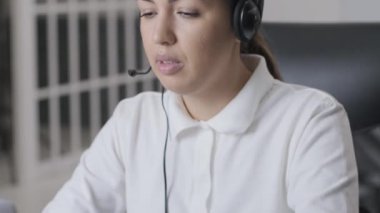 Kadın çağrı merkezi operatörü, müşteri destek acentesi kulaklık takıyor, konsültasyon yapıyor, dizüstü bilgisayarda yazıyor, internette konuşuyor, yardım hattı operatörü konferans videosu çekiyor.