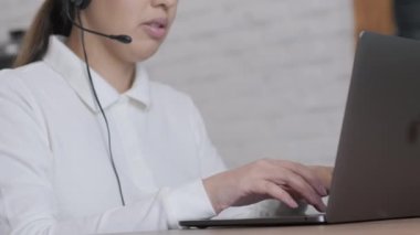 Kadın çağrı merkezi operatörü, müşteri destek acentesi kulaklık takıyor, konsültasyon yapıyor, dizüstü bilgisayarda yazıyor, internette konuşuyor, yardım hattı operatörü konferans videosu çekiyor.