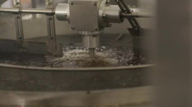 Patates cipsi ve abur cubur üretimi. Endüstriyel kızartma makinesi. Cips büyük bir kasede yağlı olarak kızartılır. Üretim fabrikası, kızartmadan sonra altın patates cipsi satıyor..