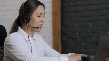 Gülümseyen kadın çağrı merkezi operatörü, müşteri destek ajanı kulaklık takıyor dizüstü bilgisayarda yazan, internet sohbeti yapan, yardım hattı operatörü, konferans videosu yapan müşteri danışmanı.