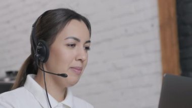 Gülümseyen kadın çağrı merkezi operatörü, müşteri destek ajanı kulaklık takıyor dizüstü bilgisayarda yazan, internet sohbeti yapan, yardım hattı operatörü, konferans videosu yapan müşteri danışmanı.