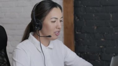 Gülümseyen kadın çağrı merkezi operatörü, müşteri destek ajanı kulaklık takıyor dizüstü bilgisayarda yazan, internet sohbeti yapan, yardım hattı operatörü, konferans videosu yapan müşteri danışmanı.