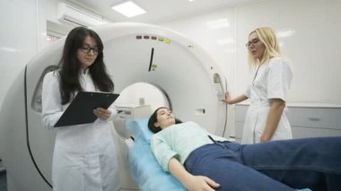 Kadın hasta, modern tıp kliniğinde iki kalifiye radyoloğun gözetiminde CT veya MRI taramasından geçiriliyor. Tomografide veya MR tarama masasında yatan hasta, makinenin dışına çıkıyor.
