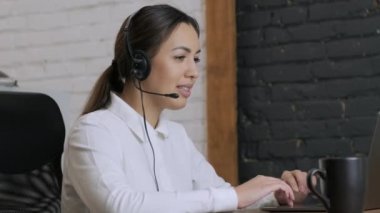 Gülümseyen kadın çağrı merkezi operatörü, müşteri destek ajanı kulaklık takıyor dizüstü bilgisayarda yazan, internet sohbeti yapan, yardım hattı operatörü, konferans videosu yapan müşteri danışmanı.