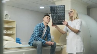 Kadın radyolog, MR taramasının sonuçlarını açıklıyor. Modern MRI tarayıcısı dışında modern klinikte görüntüler, gözlemler ve MR taramaları var.