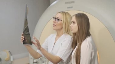 Kadın radyolog, MR taramasının sonuçlarını açıklıyor. Modern MRI tarayıcısı dışında modern klinikte görüntüler, gözlemler ve MR taramaları var.