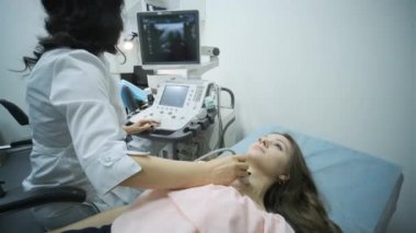 Klinikte genç kadın tiroid bezinin ultrason taraması yapılıyor. Kadın doktor hastanın boynunda ultrason sensörü çalıştırıyor..