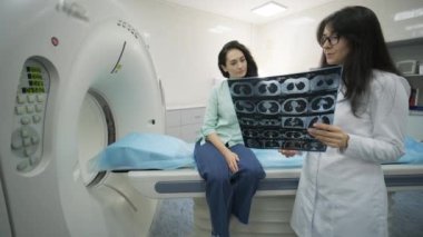 Kadın doktor radyoloji uzmanı genç bayan hasta için CT taramasının sonuçlarını açıklıyor. Modern CT tarayıcısı dışında modern klinikte tomografiyi görüntüler, gözlemler ve analiz ediyor.