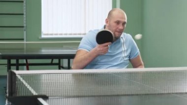 Tekerlekli sandalyedeki bir adam ping pong oynuyor. Özürlü insanlar masa tenisi oynar. Engellilerin rehabilitasyonu. Engelli sporu.