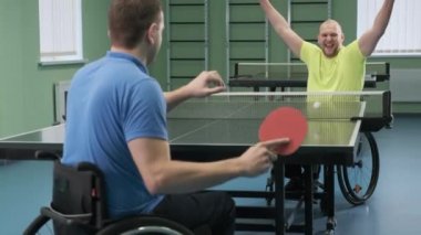 Tekerlekli sandalyedeki bir adam ping pong oynuyor. Özürlü insanlar masa tenisi oynar. Engellilerin rehabilitasyonu. Engelli sporu.