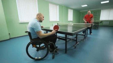 Tekerlekli sandalyedeki bir adam ping pong oynuyor. Özürlü insanlar masa tenisi oynar. Engellilerin rehabilitasyonu. Engelli sporu.