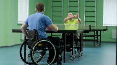 Tekerlekli sandalyedeki bir adam ping pong oynuyor. Özürlü insanlar masa tenisi oynar. Engellilerin rehabilitasyonu. Engelli sporu.