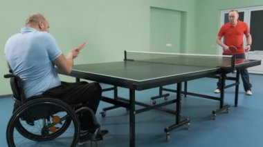 Tekerlekli sandalyedeki bir adam ping pong oynuyor. Özürlü insanlar masa tenisi oynar. Engellilerin rehabilitasyonu. Engelli sporu.