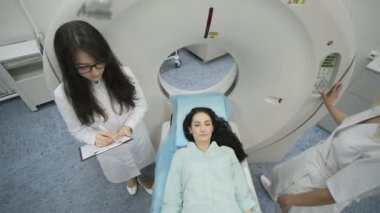 Kadın hasta, modern tıp kliniğinde iki kalifiye radyoloğun gözetiminde CT veya MRI taramasından geçiriliyor. Tomografide ya da MR tarama masasında yatan hasta makinenin içinde hareket ediyor.